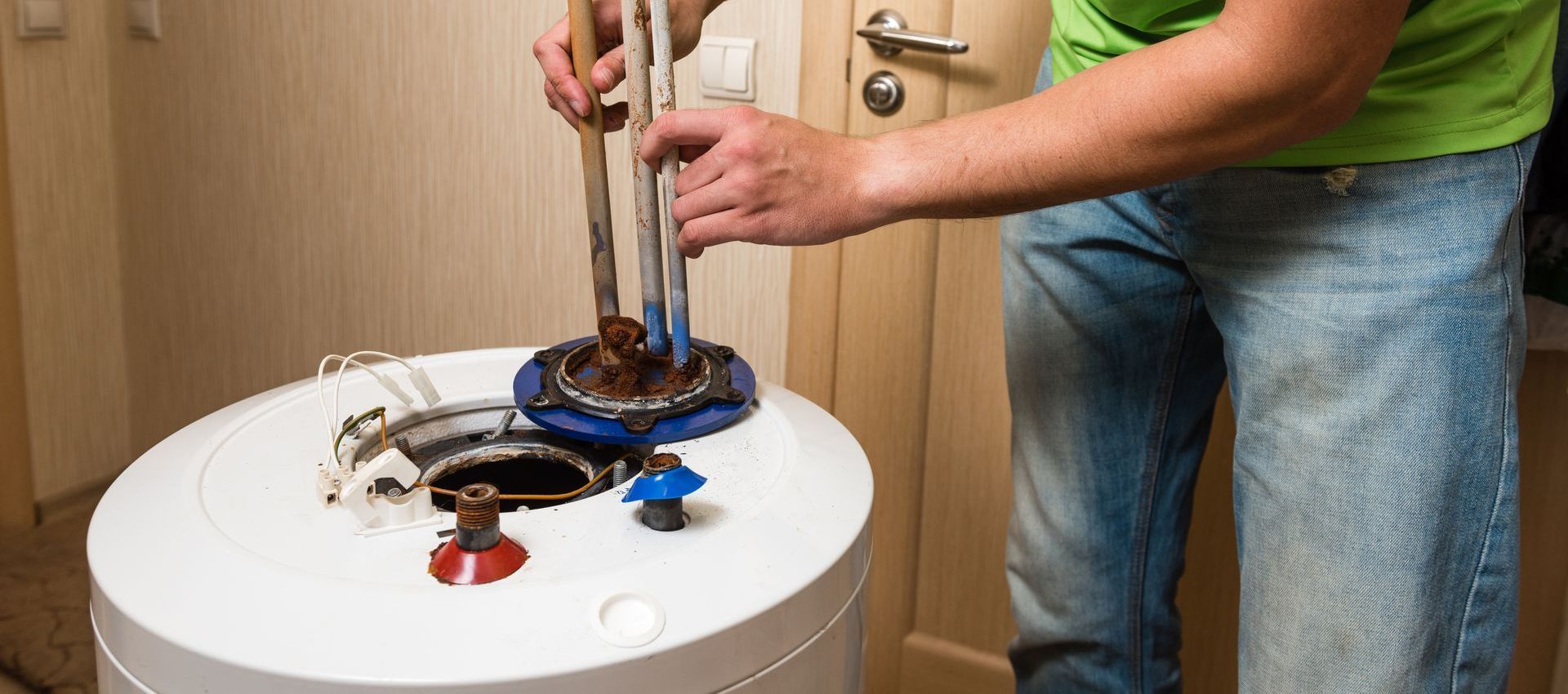 A man is fixing a water heater in a bathroom.