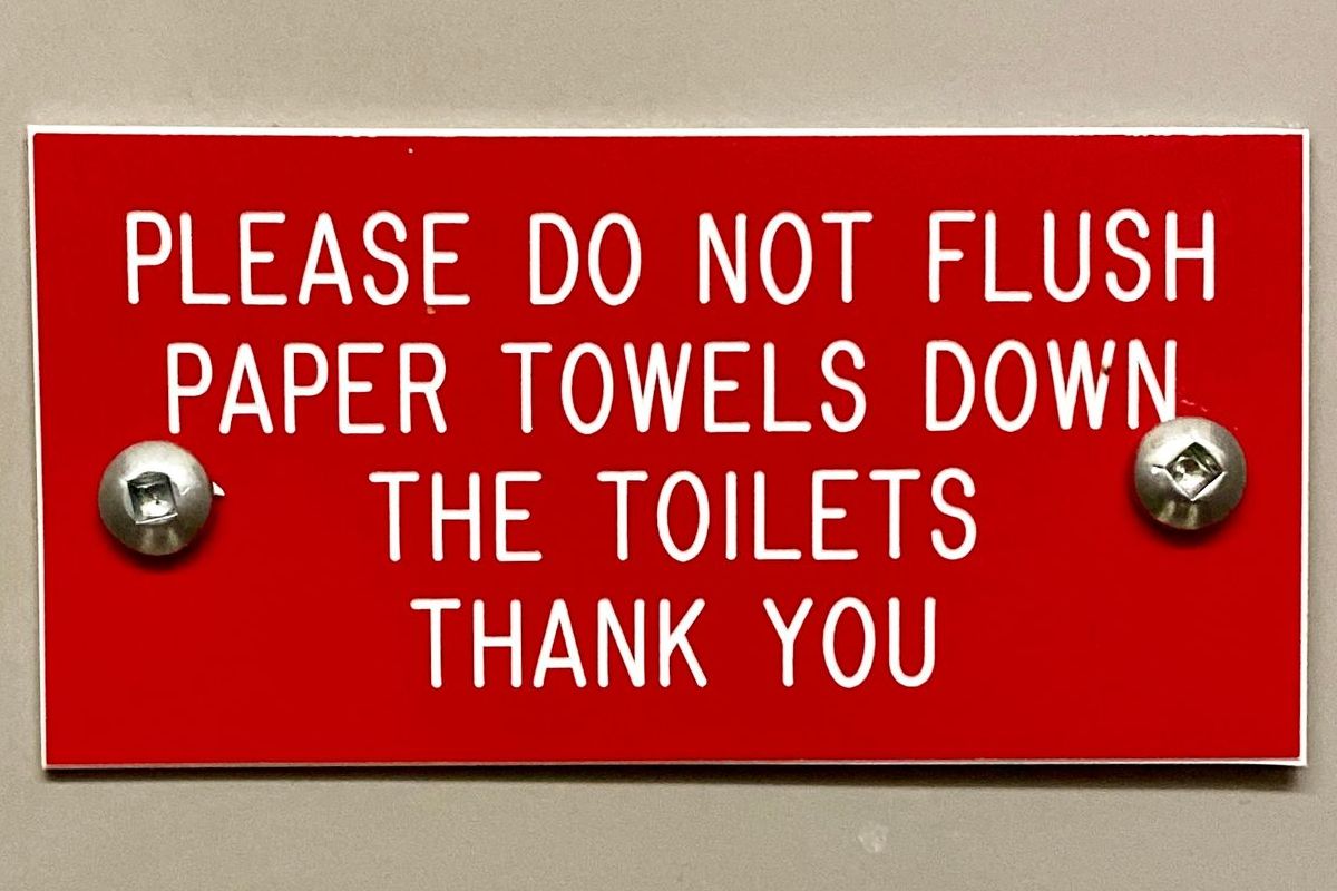 A red sign that says please do not flush paper towels down the toilets thank you