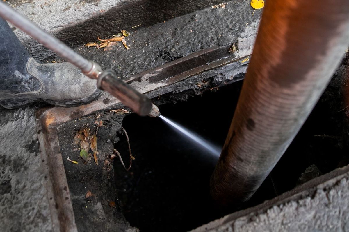 A person is using a hose to clean a drain.