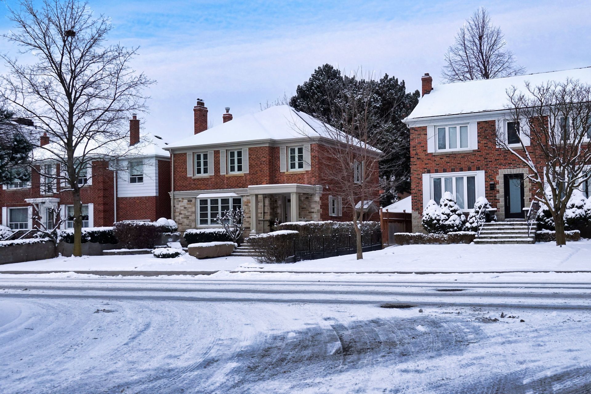 Snow-covered suburban homes on a winter day. Red brick houses with white trim and bare trees.