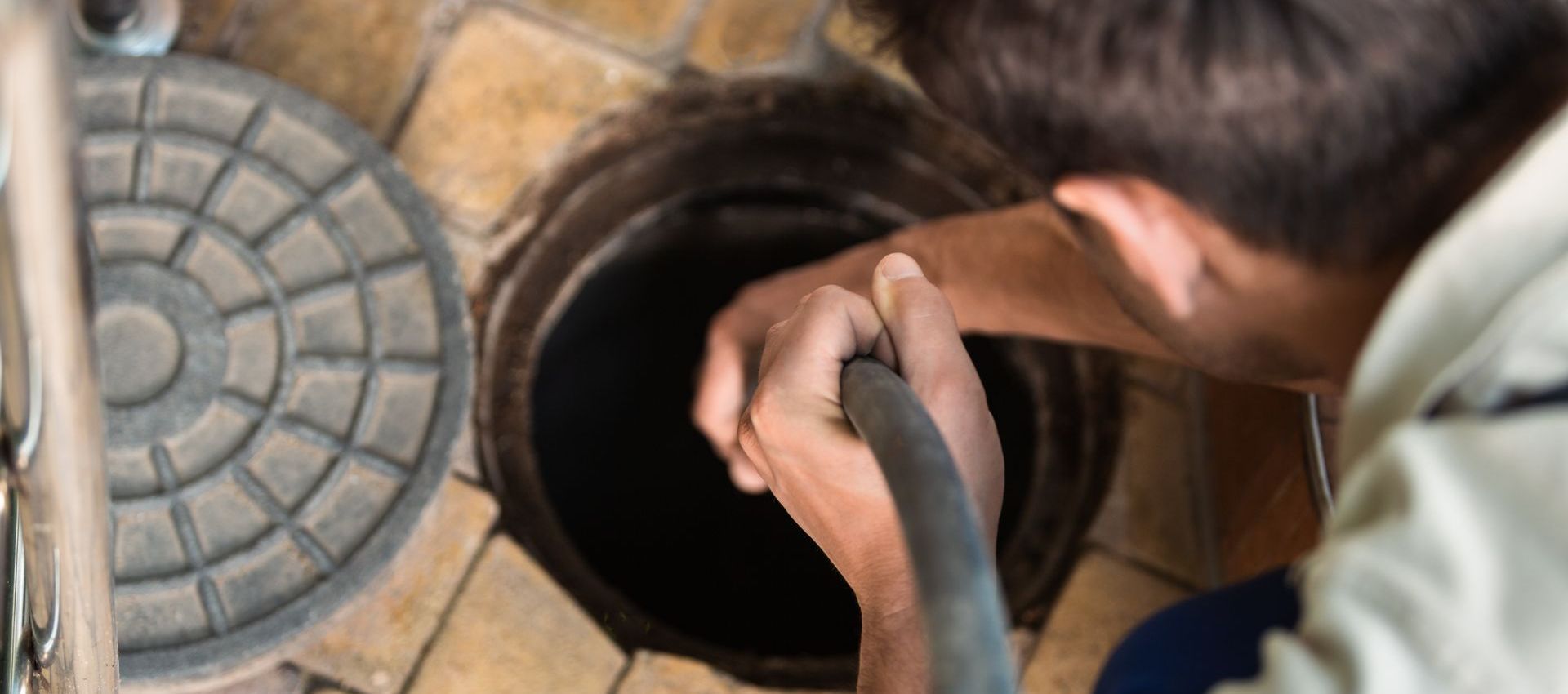 A man is cleaning a manhole cover with a hose.