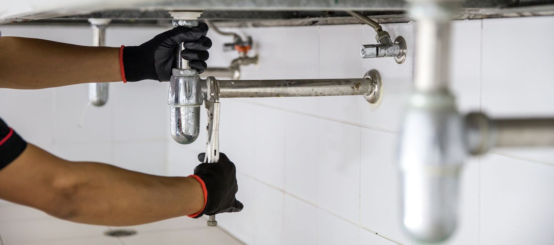 A plumber is fixing a sink with a wrench.