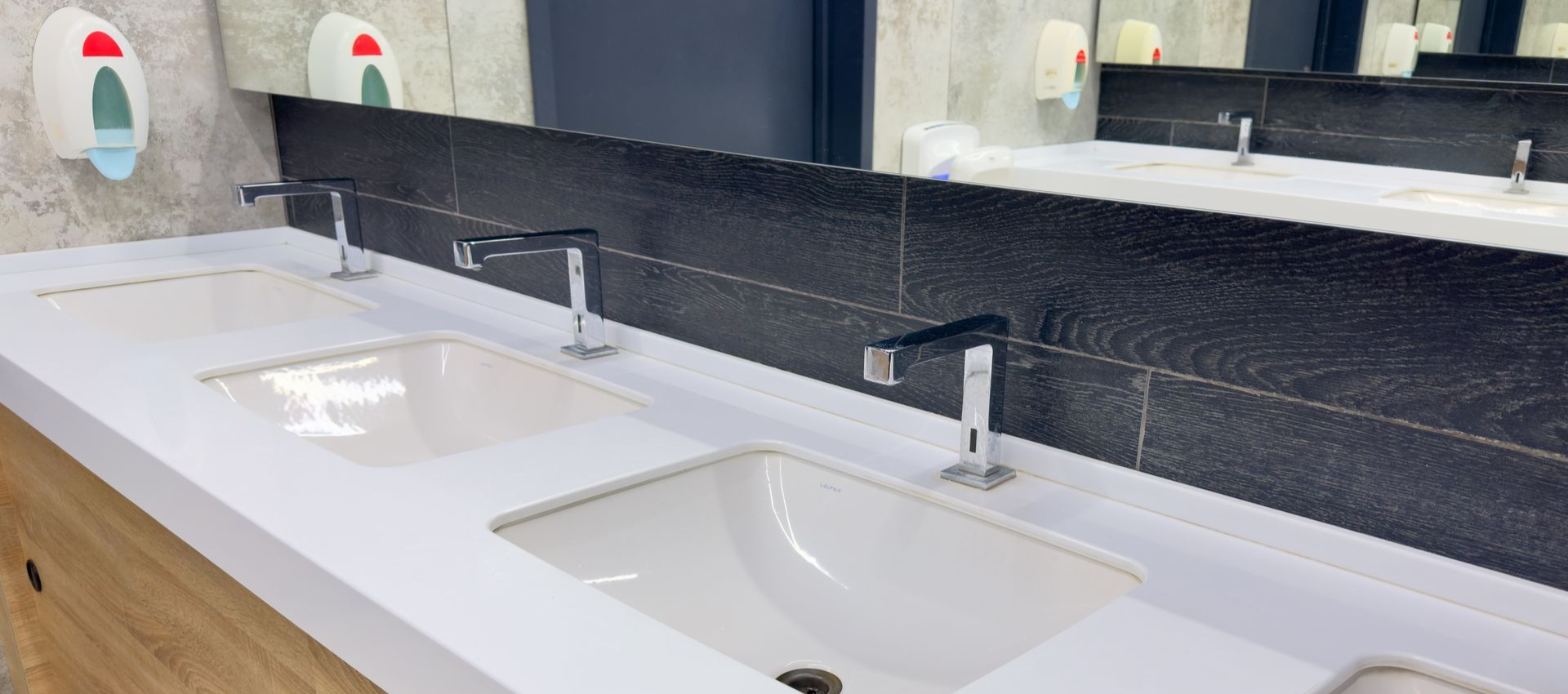 Bathroom sinks with chrome faucets and soap dispensers above a wooden cabinet, large mirror.