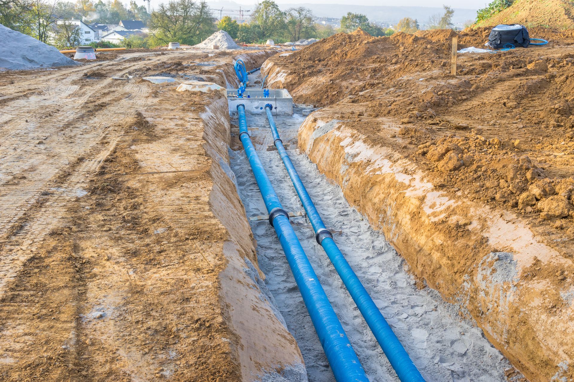 A bunch of blue pipes are laying in the dirt on a construction site.