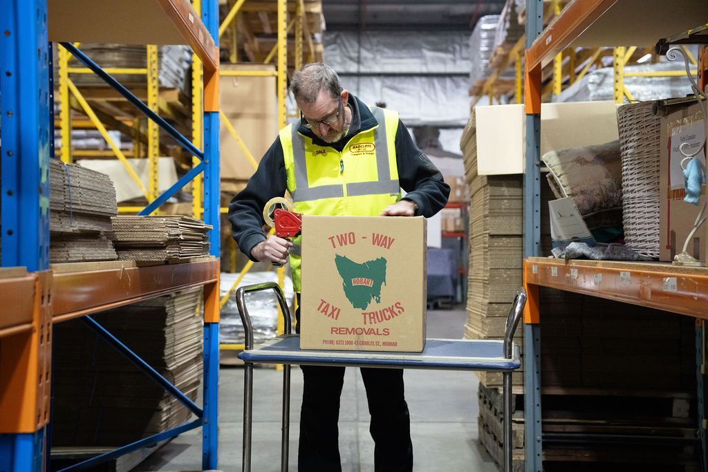 A man is kneeling down in front of a stack of boxes in a warehouse.