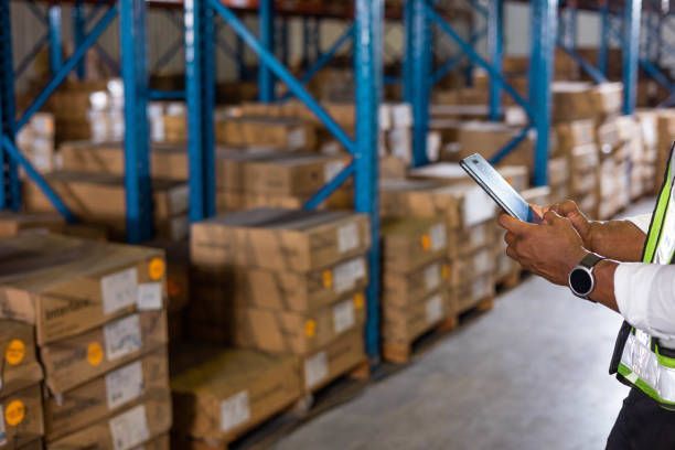 Worker using handheld device in warehouse with boxes.