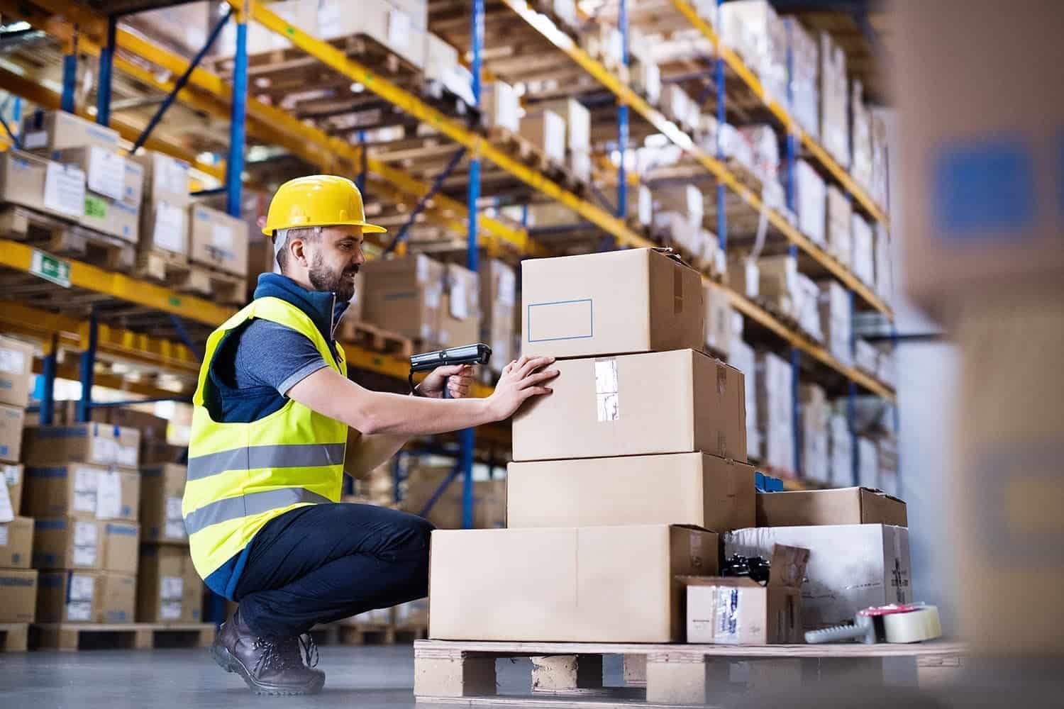 A man is kneeling down in front of a stack of boxes in a warehouse.