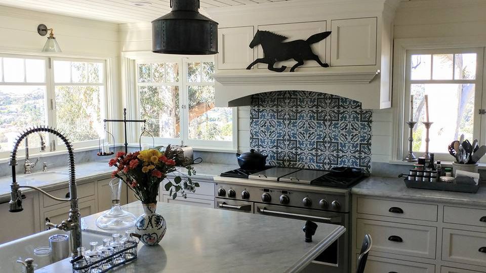 Bright, white kitchen with island, range, and windows; a decorative horse above the stove.