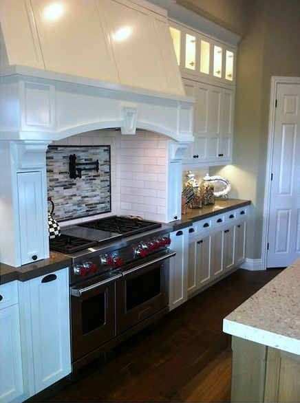Elegant white kitchen with stainless steel stove, range hood, and tile backsplash.
