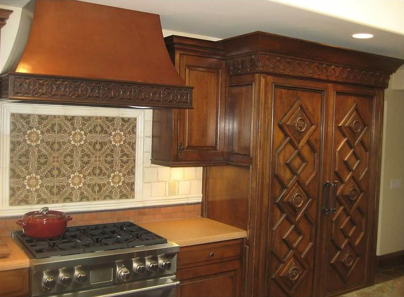 Kitchen with ornate, dark wood cabinetry, copper range hood, and tile backsplash.