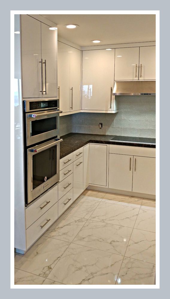 White modern kitchen with glossy cabinets, stainless steel appliances, and marble-like floors.