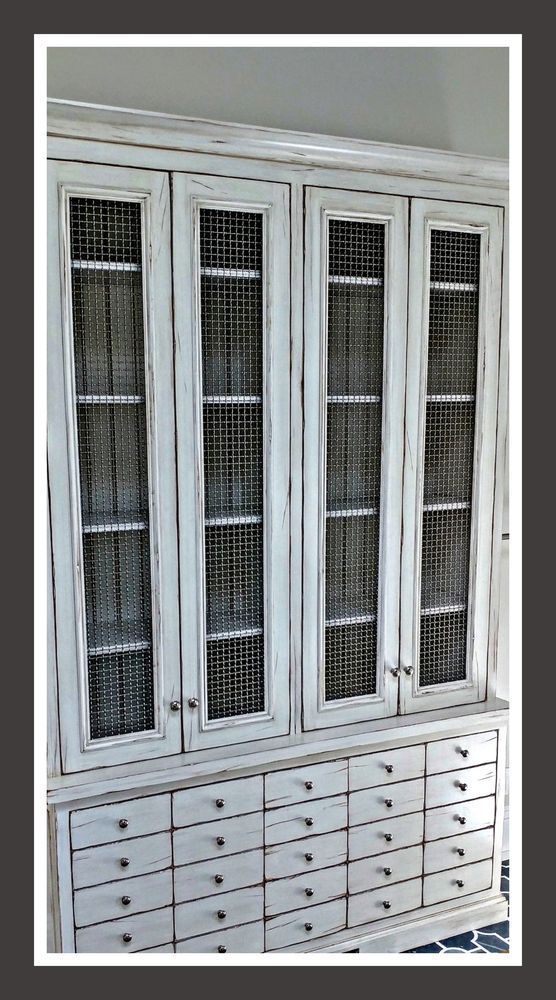 White cabinet with multiple drawers and mesh-fronted upper doors, distressed finish.