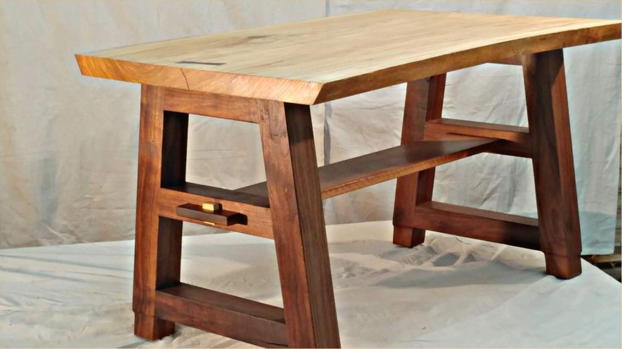 Wooden desk with a light-colored top and dark brown legs and a lower shelf, set against a white backdrop.