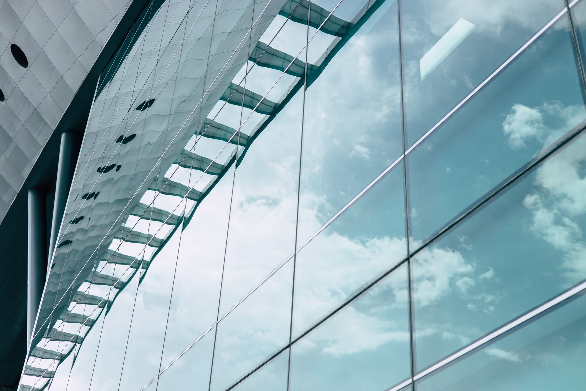 Glass facade of a modern building reflecting a cloudy sky and metal structure