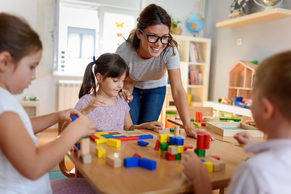 Teacher Helping Children Build With Blocks in a Brightly Lit Classroom — Five Star Family Day Care in Metford, NSW