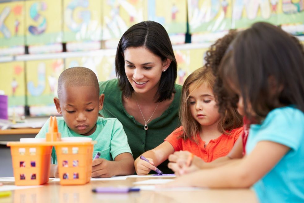 Teacher With Children, Assisting With Drawing at a Table in a Classroom — Five Star Family Day Care in Metford, NSW