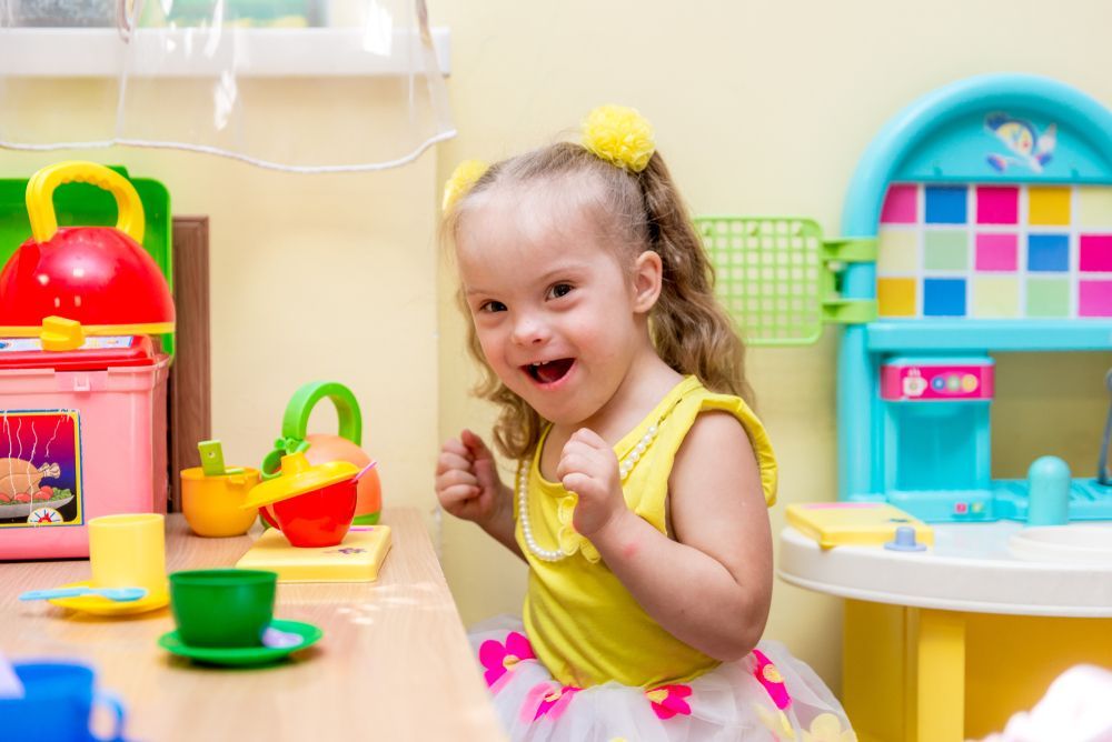Girl With Down Syndrome Smiles at a Toy Kitchen — Five Star Family Day Care in Newcastle, NSW