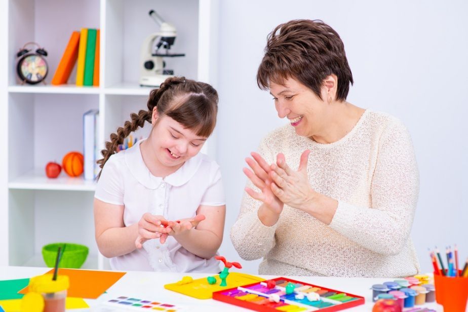 Woman and Girl With Down Syndrome Smiling While Crafting at a Table — Five Star Family Day Care in Newcastle, NSW