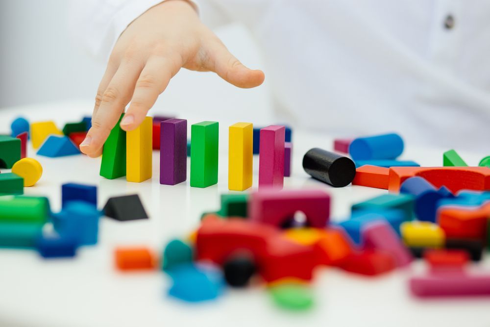 Child's Hand Playing With Colorful Wooden Blocks on a White Table