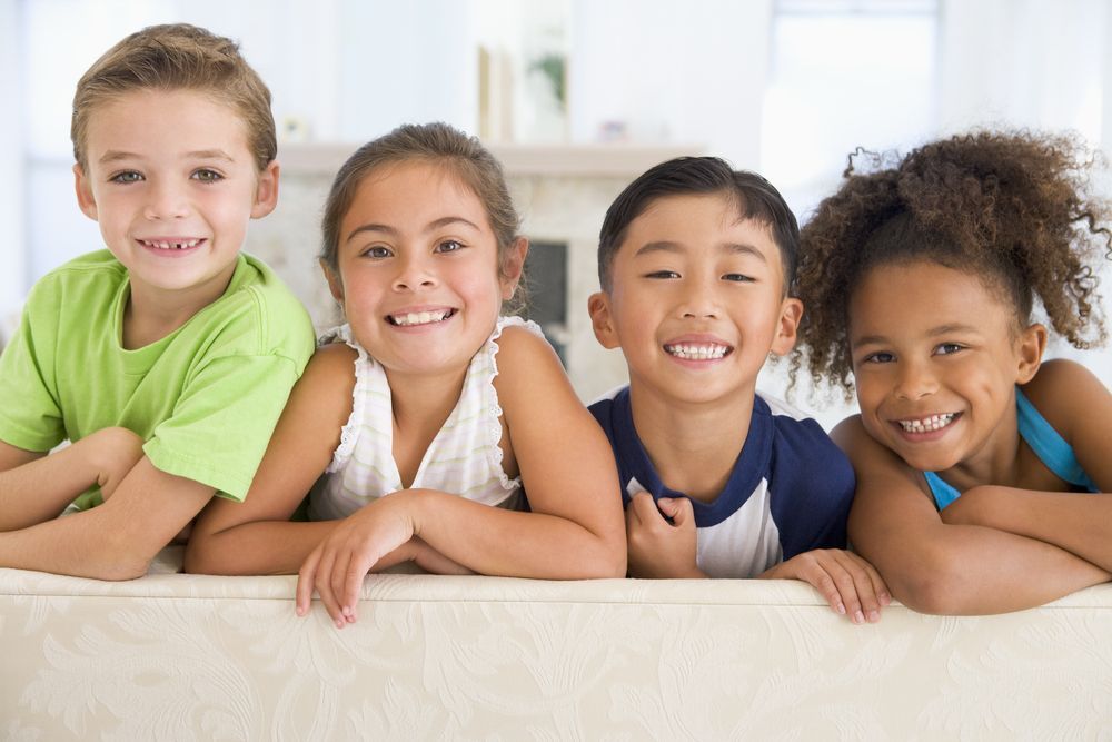 Four Diverse Children Smiling, Leaning on a Couch — Five Star Family Day Care In Metford, NSW