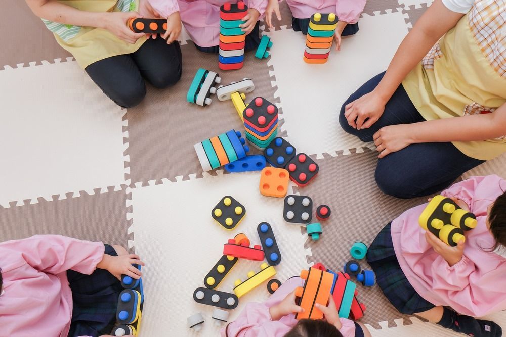 A Group of Children Are Sitting on the Floor Playing With Toys — Five Star Family Day Care in Muswellbrook, NSW