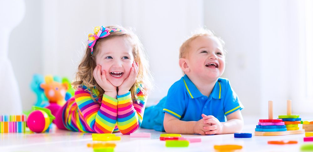 Two Smiling Children Playing on a White Floor With Colorful Toys — Five Star Family Day Care In Metford, NSW