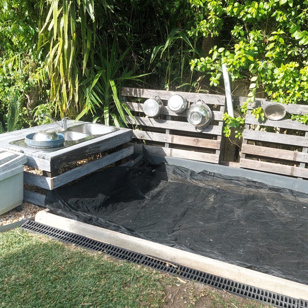 Outdoor Sink Area with Pallets, Black Mat, Drainage, and Hanging Metal Bowls — Five Star Family Day Care in Maitland, NSW