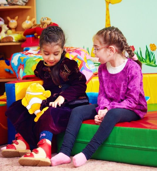 Two Young Girls Sitting Indoors and Smiling — Five Star Family Day Care in Metford, NSW