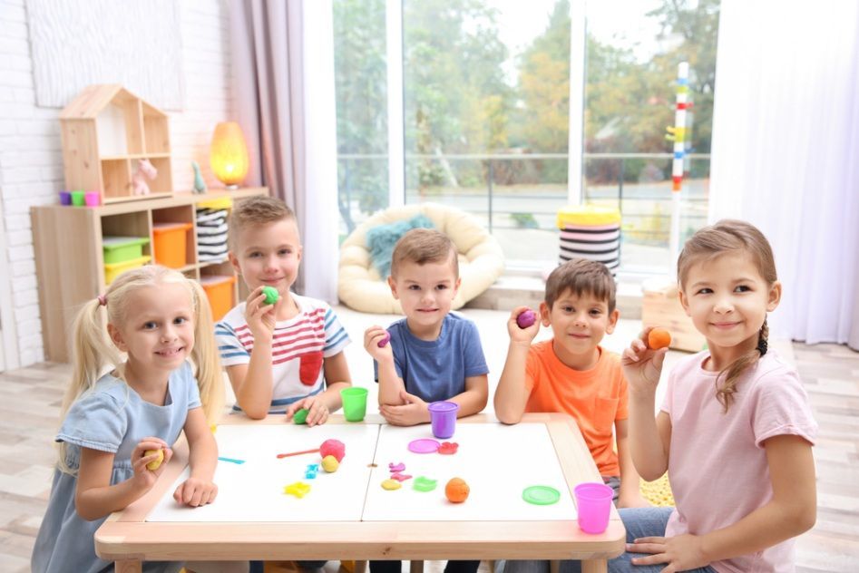 Five Children Sitting Around a Table, Smiling While Playing — Five Star Family Day Care in Newcastle, NSW