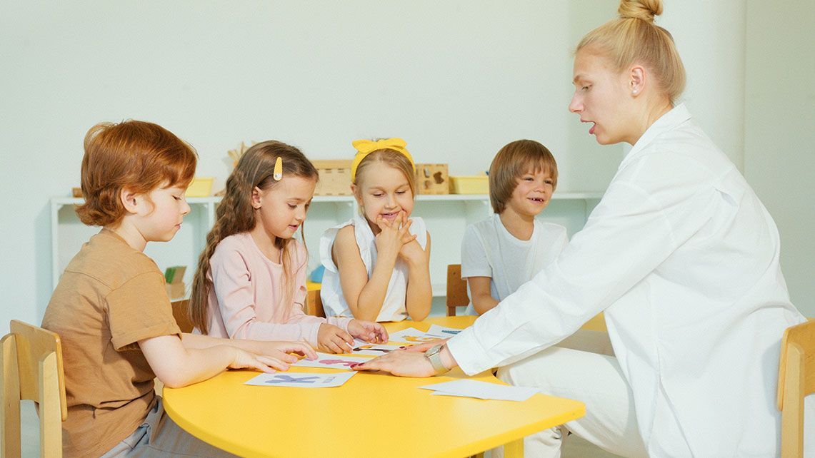 A Group of Children Are Sitting at a Table Painting With a Teacher — Five Star Family Day Care in Maitland, NSW