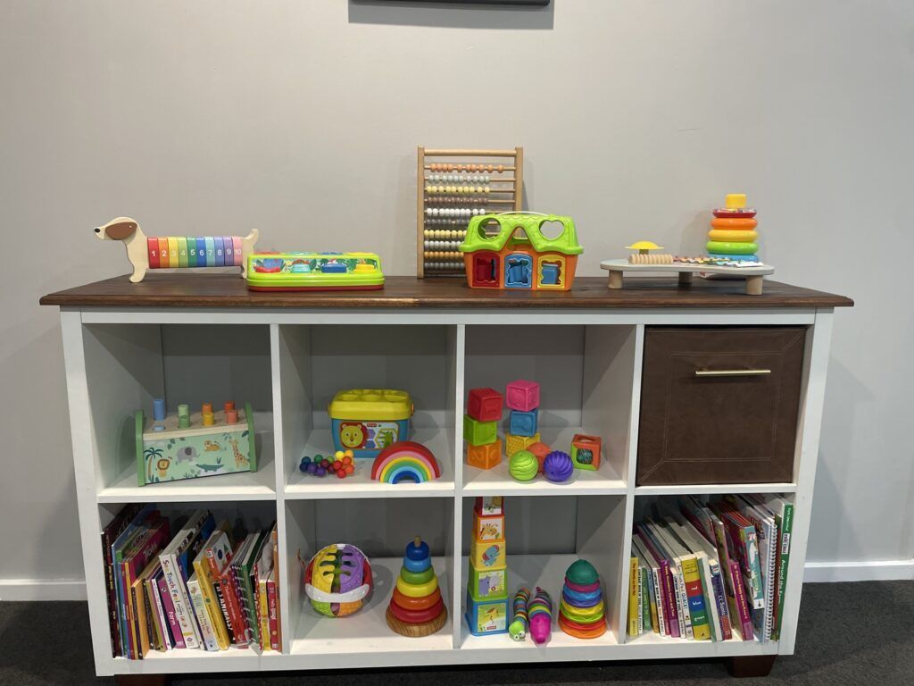White and Brown Toy Shelf Filled With Colorful Toys and Books Against a Wall — Five Star Family Day Care In Muswellbrook, NSW