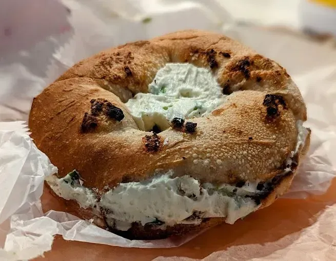 A toasted bagel with cream cheese, on a paper wrapper.