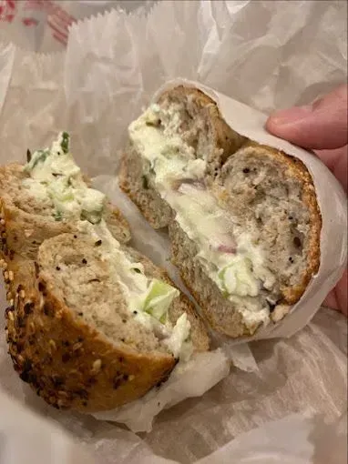 Bagel sandwich cut in half, filled with cream cheese, cucumbers, and scallions; wrapped in paper.