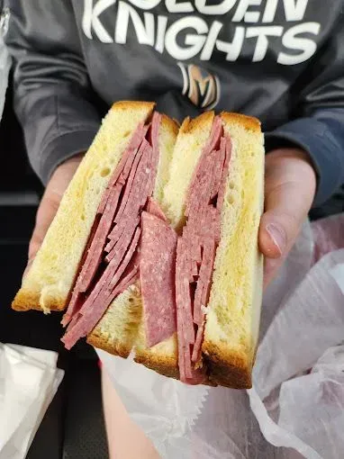 A person holding a thick sandwich of sliced meat between two slices of toasted bread.