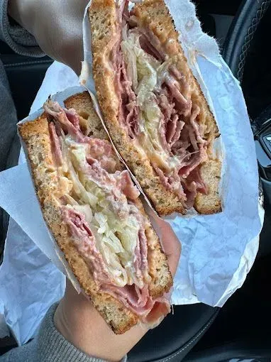 Two halves of a large Reuben sandwich on toasted bread, held in hands.