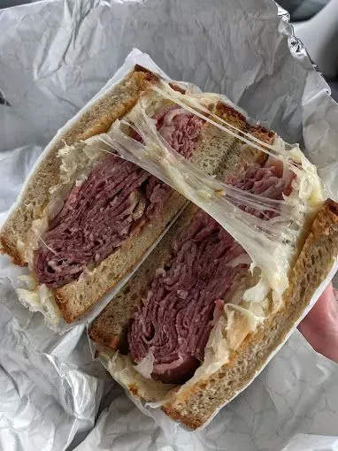 Reuben sandwich, sliced in half, oozing melted cheese. Corned beef, sauerkraut, rye bread.