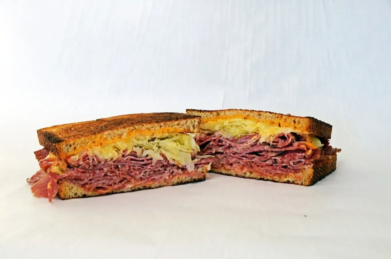 Reuben sandwich cut in half, showing corned beef, sauerkraut, cheese, and rye bread.