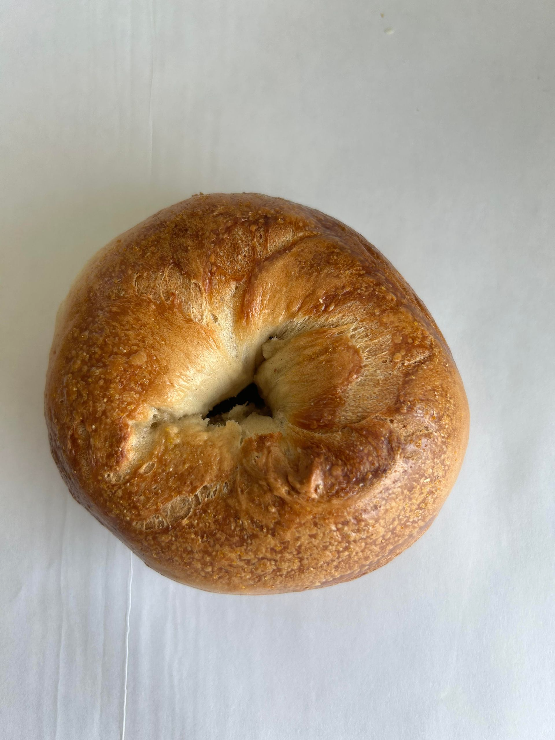 Close-up of a golden-brown bagel with a hole, set on a white surface.