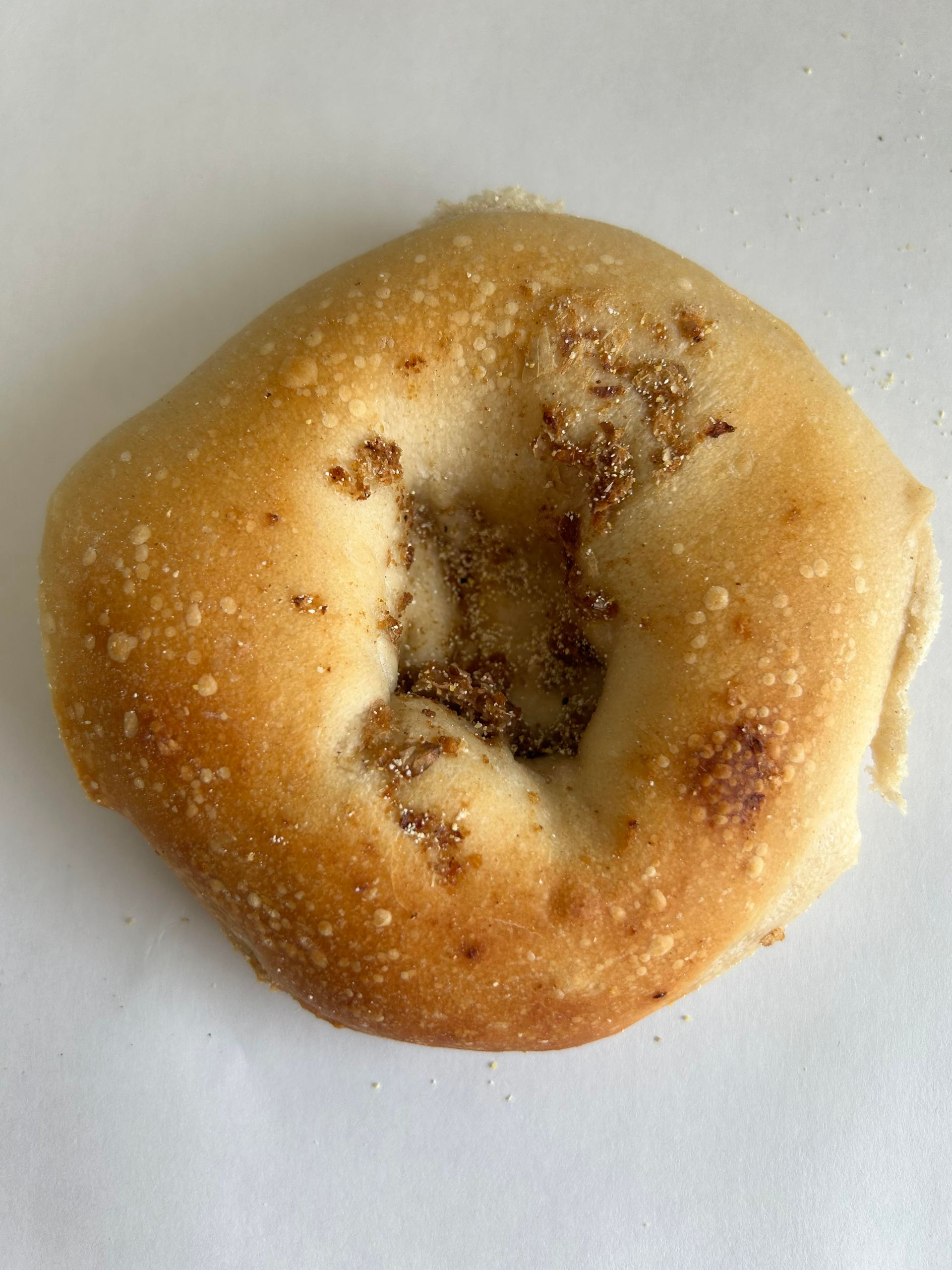 Close-up of a round, golden-brown bagel with a visible hole. It sits on a white surface.