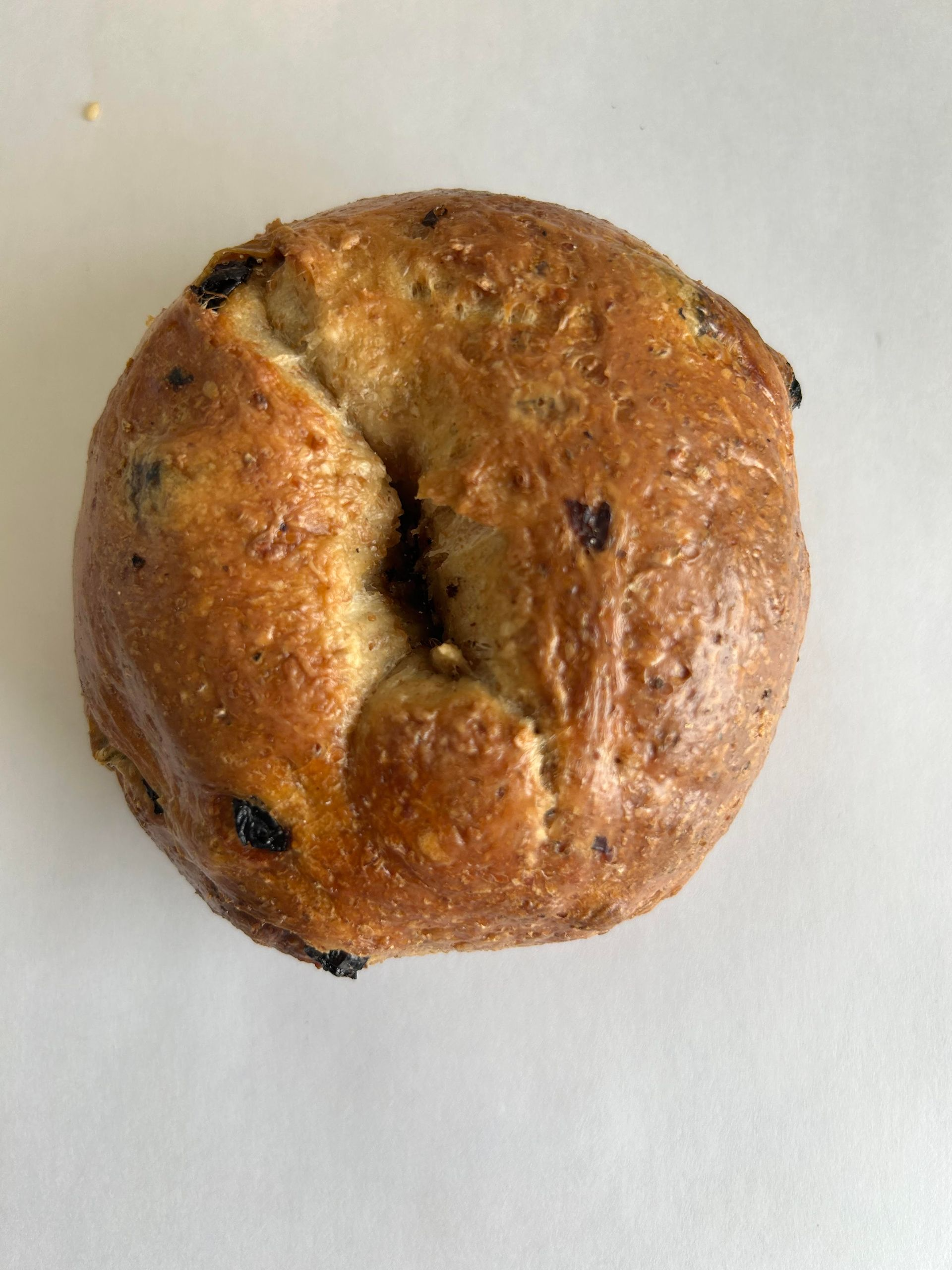 Top-down view of a toasted, golden-brown raisin bagel on a white surface.