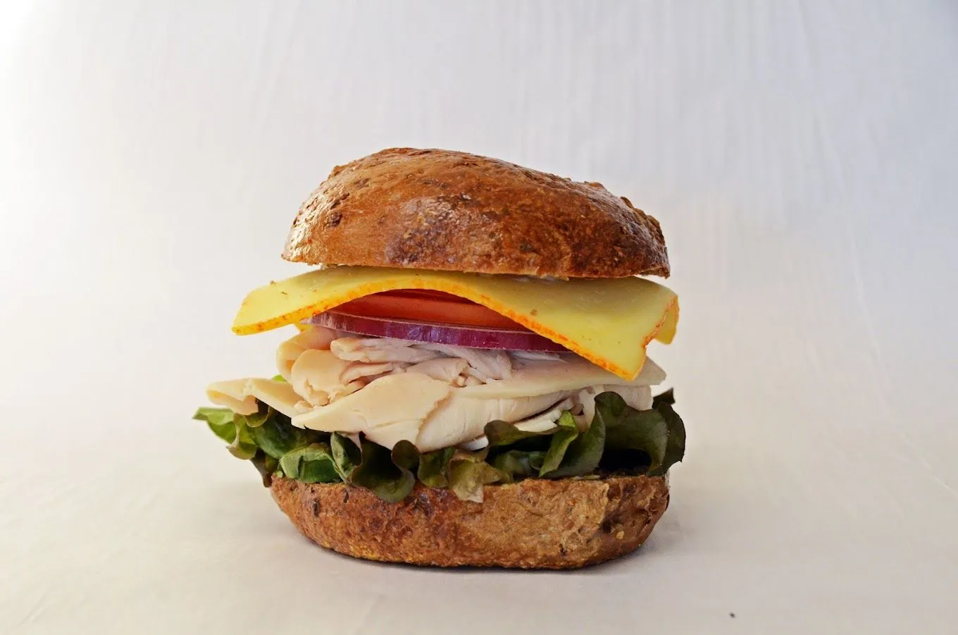 Turkey and cheese sandwich on a rustic bun with lettuce, tomato, and onion.