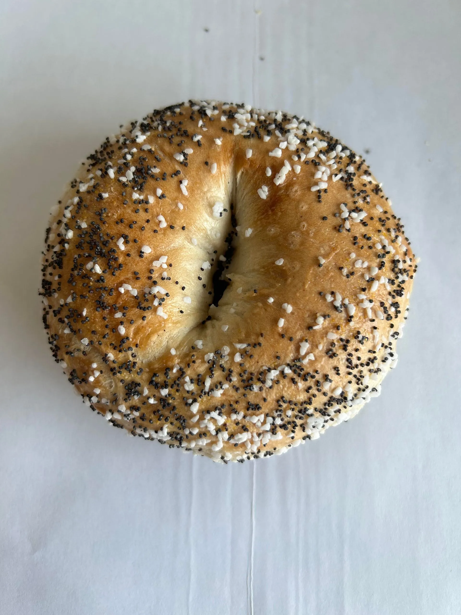 Everything bagel on a white surface, sprinkled with poppy seeds, salt, and a slightly golden color.