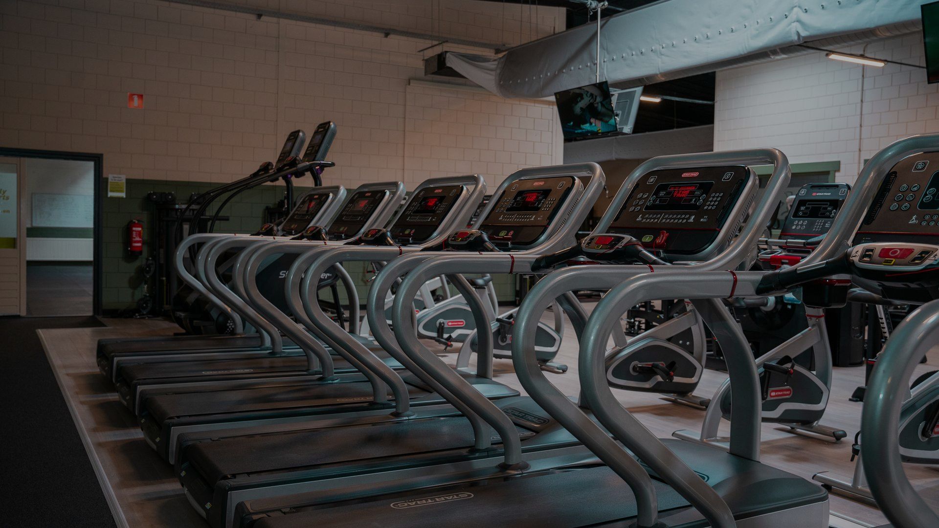In een sportschool staan een aantal loopbanden op een rij.