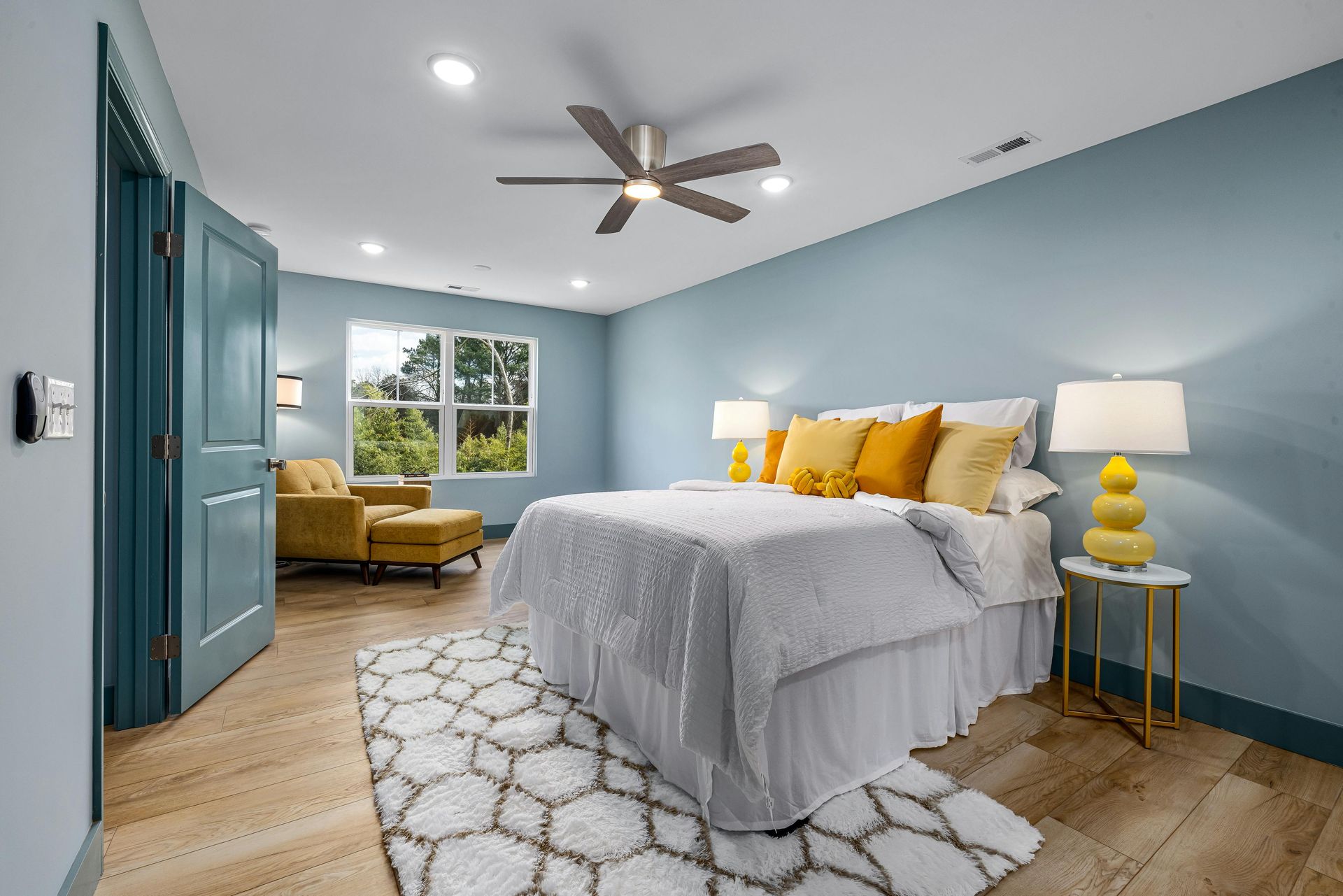 A bedroom with a bed , ceiling fan , lamps , and a rug.