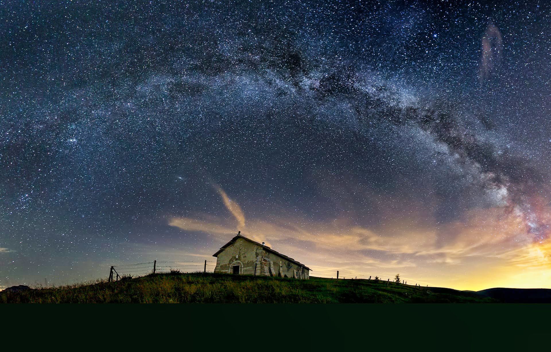 Una piccola casa è situata in cima ad una collina sotto un cielo notturno stellato.