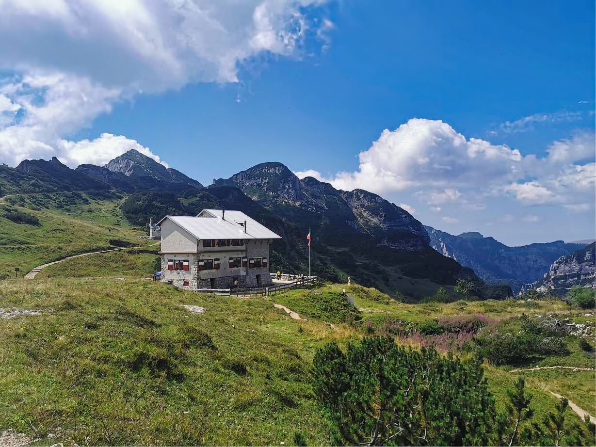 Una casa è situata in cima ad una collina erbosa tra le montagne.