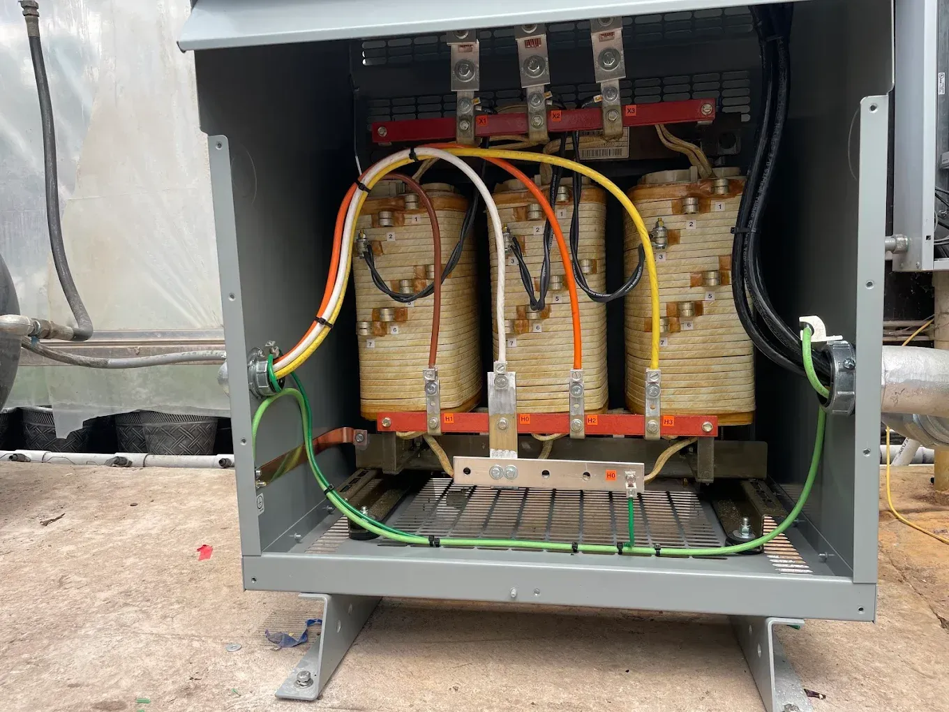 Open electrical transformer with copper windings, gray enclosure, and wiring.