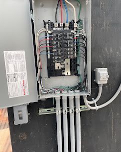 Electrical panel with wiring and conduits. Gray metal box mounted on a wall.
