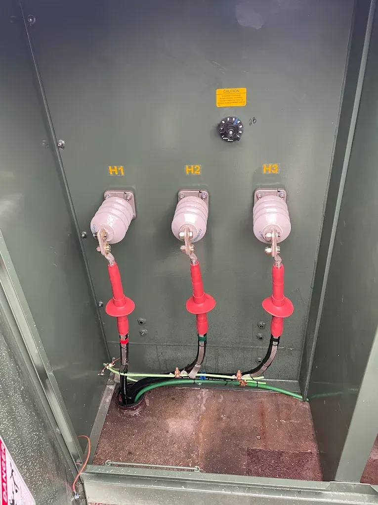 Green electrical cabinet with three high voltage cable connections labeled H1, H2, H3 and a yellow warning label.