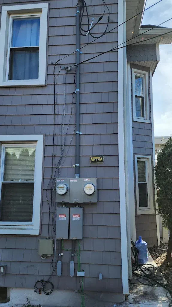 Grey siding with electrical meters and conduit on the outside of a house.